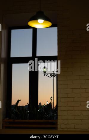 Eine ruhige und ruhige Abendszene, die durch ein Fenster betrachtet wird und eine Straßenlaterne und einen wunderschönen Sonnenuntergang zeigt Stockfoto