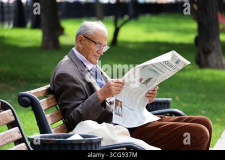 Moskau, Russland - 26. August 2025: Ein alter Mann liest russische Zeitung auf der Straßenbank der Stadt Stockfoto