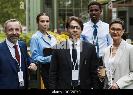 Gruppe von verschiedenen Geschäftsleuten, darunter weiße, schwarze Manager und Führungskräfte, die draußen mit Konferenzabzeichen stehen und in die Kamera schauen Stockfoto