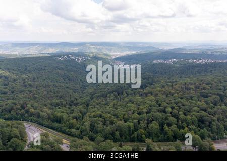 Aus der Vogelperspektive auf einen üppig grünen Wald mit einer kurvenreichen Straße, die an eine Wohngegend der Stuttgarter Stadt grenzt. Die Szene fängt die Interse ein Stockfoto