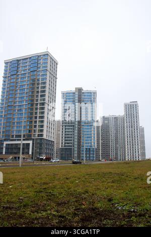 Weißrussland, Minsk - 26, 12, 2024: Im Vordergrund gibt es ein üppiges grasbewachsenes Feld, im Hintergrund eine Reihe von hohen Strukturen, die bis zu Towa reichen Stockfoto