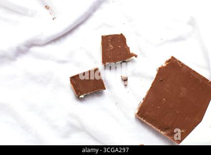 Tafelschokolade aus Milchschokolade mit Keksen und Cremefüllung auf weißem Stoff, die das Konzept von Wäsche oder Schmutz darstellen. Hausarbeit und Haushaltskonzept Stockfoto