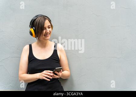 Fröhliche blonde Frau 40er in gelben Kopfhörern lächelt mit geschlossenen Augen und hört Musik Stockfoto