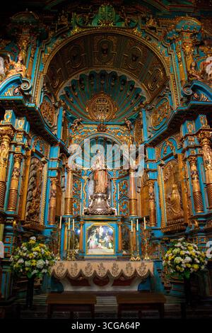 Innenraum der Kathedrale mit gewölbten Decken, goldenen Rippen, verzierten Altar, Holzbänken, Kronleuchtern, karierter Boden und symmetrische Architektur Stockfoto