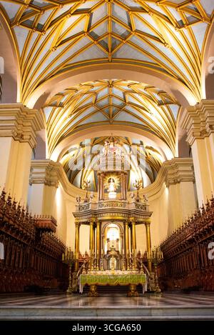 Innenraum der Kathedrale mit gewölbten Decken, goldenen Rippen, verzierten Altar, Holzbänken, Kronleuchtern, karierter Boden und symmetrische Architektur Stockfoto