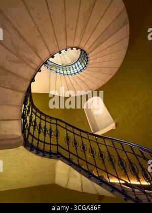 Elegante Wendeltreppe umgeben von goldfarbenen Wänden mit kunstvollem Eisengeländer, von oben betrachtet. Stockfoto