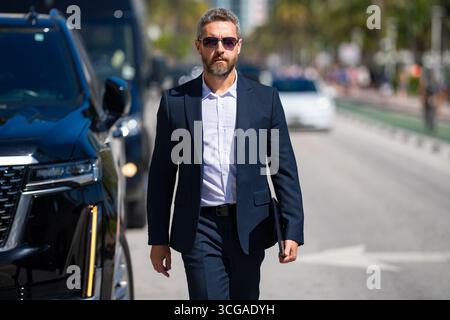 Reiche Geschäftsleute im Freien. Ein reicher Geschäftsmann genießt seinen Erfolg. Luxuriöser Geschäftsmann in elegantem Anzug. Reicher Mann vor einem teuren Auto. Luxusunternehmen Stockfoto