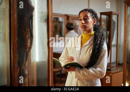 Junge Erwachsene Frau, die Museumsausstellung beobachtet und Notizen in Notizbuch macht Stockfoto