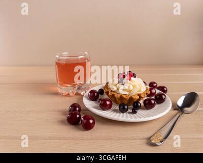 Eine köstliche Desserttarte mit Schlagsahne und gemischten Beeren, begleitet von einem Glas Saft und einem Löffel auf einem Holztisch Stockfoto