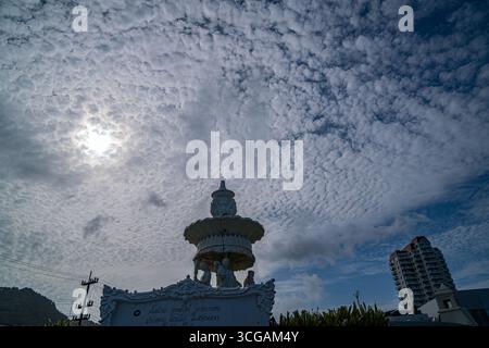 Phuket Thailand. 13. August 2025: Vor dem Hintergrund von weichen, strukturierten Wolken erhebt sich eine weiße Skulptur mit Eleganz, die menschliche Kunst mit Natur verbindet Stockfoto