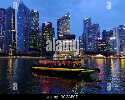 Malerische Skyline Singapurs nach Sonnenuntergang mit beleuchteten Wolkenkratzern und Booten auf dem Wasser Stockfoto