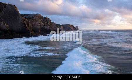 Wellen brechen bei Sonnenuntergang an der felsigen Küste von Sintra, Portugal Stockfoto