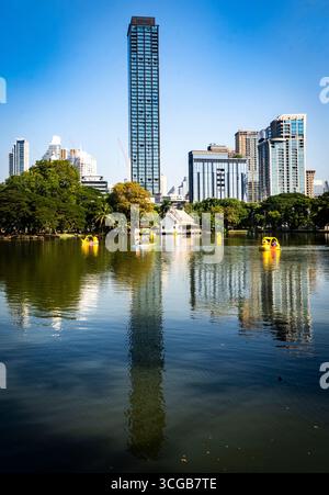 Eine ruhige urbane Parkszene mit einem ruhigen See, der hohe Gebäude reflektiert, und einem klaren blauen Himmel, mit Paddelbooten auf dem Wasser Stockfoto