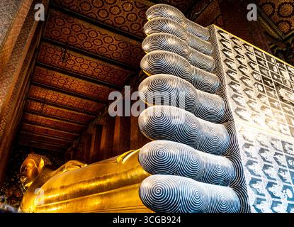 Aus nächster Nähe sehen Sie die Füße einer liegenden goldenen buddha-Statue mit komplizierten Mustern und Designs in einem reich verzierten Tempelinneren Stockfoto
