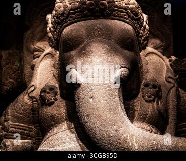 Aus nächster Nähe sehen Sie eine Steinskulptur einer elefantenköpfigen Gottheit mit komplizierten Schnitzereien und Texturen, mit dramatischer Beleuchtung Stockfoto