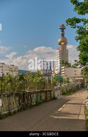 Blick von der Sonne auf Wiens Müllkraftwerk Spittelau mit goldener Kuppel von Hundertwasser. Vordergrund: Fußgängerweg und farbenfroher Graffiti-Zaun Stockfoto
