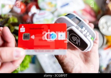 Bayern, Deutschland - 27. August 2025: Eine rote Sparkasse Girocard wird an einem Zahlungsterminal gehalten, um im Supermarkt kontaktlos zu bezahlen. Symbolisches Bild bargeldloser Zahlungsvorgänge im Alltag *** eine rote Sparkassen-Girocard wird an ein Bezahlterminal halten, um den Einkauf im Supermarkt kontaktlos zu bezahlen. Symbolbild bargeldloser Zahlungsvorgang im Alltag Stockfoto