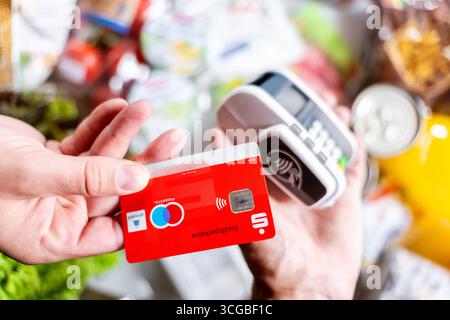 Bayern, Deutschland - 27. August 2025: Eine rote Sparkasse Girocard wird an einem Zahlungsterminal gehalten, um im Supermarkt kontaktlos zu bezahlen. Symbolisches Bild bargeldloser Zahlungsvorgänge im Alltag *** eine rote Sparkassen-Girocard wird an ein Bezahlterminal halten, um den Einkauf im Supermarkt kontaktlos zu bezahlen. Symbolbild bargeldloser Zahlungsvorgang im Alltag Stockfoto