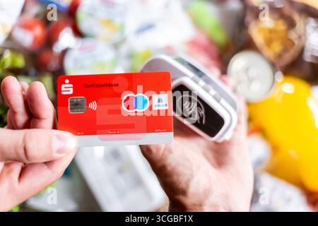 Bayern, Deutschland - 27. August 2025: Eine rote Sparkasse Girocard wird an einem Zahlungsterminal gehalten, um im Supermarkt kontaktlos zu bezahlen. Symbolisches Bild bargeldloser Zahlungsvorgänge im Alltag *** eine rote Sparkassen-Girocard wird an ein Bezahlterminal halten, um den Einkauf im Supermarkt kontaktlos zu bezahlen. Symbolbild bargeldloser Zahlungsvorgang im Alltag Stockfoto