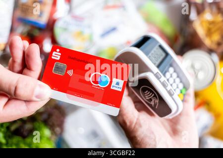 Bayern, Deutschland - 27. August 2025: Eine rote Sparkasse Girocard wird an einem Zahlungsterminal gehalten, um im Supermarkt kontaktlos zu bezahlen. Symbolisches Bild bargeldloser Zahlungsvorgänge im Alltag *** eine rote Sparkassen-Girocard wird an ein Bezahlterminal halten, um den Einkauf im Supermarkt kontaktlos zu bezahlen. Symbolbild bargeldloser Zahlungsvorgang im Alltag Stockfoto