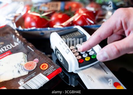 Bayern, Deutschland - 27. August 2025: Ein Kunde bezahlt seine Lebensmittel im Supermarkt mit einer Kreditkarte und gibt die PIN am Terminal ein *** ein Kunde bezahlt seinen Lebensmitteleinkauf im Supermarkt mit einer Kreditkarte und gibt die PIN am Terminal ein Stockfoto