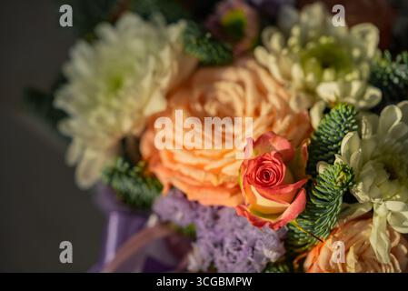 Lebendiges Blumenstrauß mit zarten Rosenknospen, die aus einem Bett aus orangen Rosen, weißen Chrysanthemen und lila Lisianthus hervorgehen, was eine wunderschöne Farbgebung und Textur schafft Stockfoto