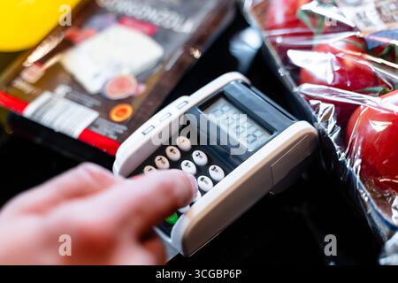 Bayern, Deutschland - 27. August 2025: Ein Kunde gibt seine PIN am Kartenleser an der Kasse des Supermarkts ein. Illustration bargeldloser Kartenzahlung beim Einkaufen von Lebensmitteln. *** Ein Kunde gibt an der Supermarktkasse seine PIN am Kartenlesegerät ein. Darstellung des bargeldlosen Bezahlens mit Karte beim Einkauf von Lebensmitteln. Stockfoto
