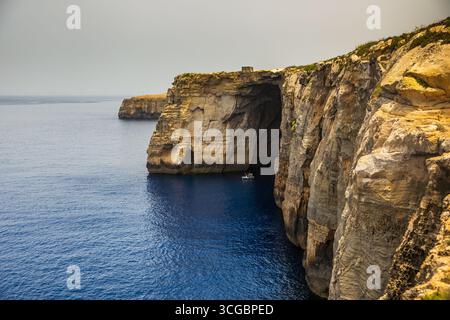 Gozo, Malta – 23. Juni 2021: Kleines Boot mit Menschen in der Nähe von hoch aufragenden Kalksteinklippen entlang der Mittelmeerküste. Stockfoto