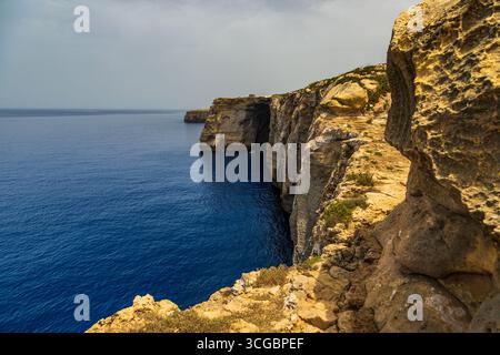 Gozo, Malta – 23. Juni 2021: Kleines Boot mit Menschen in der Nähe von hoch aufragenden Kalksteinklippen entlang der Mittelmeerküste. Stockfoto