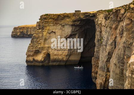 Gozo, Malta – 23. Juni 2021: Kleines Boot mit Menschen in der Nähe von hoch aufragenden Kalksteinklippen entlang der Mittelmeerküste. Stockfoto