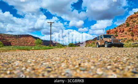 Jeep Wrangler auf der Desert Road mit Red Rock Mesas und dramatischen Wolken im Erdgeschoss Stockfoto