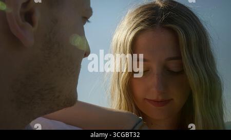 Die junge Frau schaut einen Mann in einer Nahaufnahme im Freien emotional an, während warmes Sonnenlicht und Lichtreflexe die Stimmung verbessern. Stockfoto
