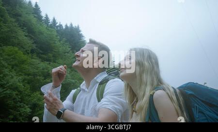 Junge Paare mit Rucksäcken wandern durch einen nebeligen Wald, schauen nach oben und genießen die Natur und Abenteuer an einem nebeligen Tag. Stockfoto