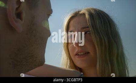 Frau schaut einen Mann emotional in einer Nahaufnahme im Freien an, während warmes Sonnenlicht und Lichtreflexe die Stimmung verbessern. Stockfoto