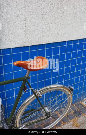 Grünes Vintage-Fahrrad mit braunem Ledersattel, geparkt an einer blauen Wand auf einer Straße Stockfoto