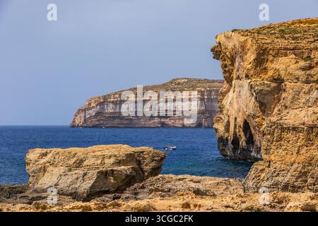 Gozo, Malta – 23. Juni 2021: Kleines Boot mit Menschen, die in der Nähe von Kalksteinklippen entlang der zerklüfteten Mittelmeerküste segeln. Stockfoto