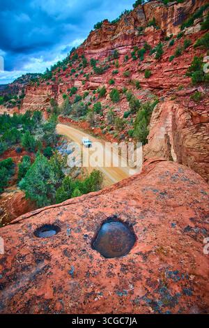 Gewundene Dirt Road durch den Red Rock Canyon mit White SUV und Rain Pools Utah Stockfoto
