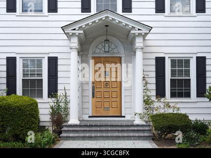 Traditionelles zweistöckiges weißes Schalenhaus mit Holzmaserung-Eingangstür Stockfoto
