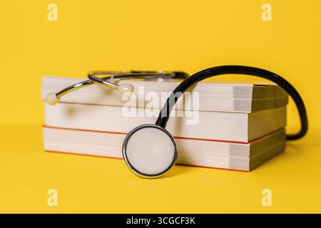 Stethoskop auf gestapelten Lehrbüchern vor hellgelbem Hintergrund. Medizinische Ausbildung. Stockfoto