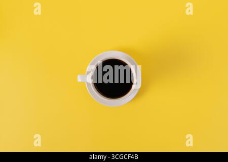 Weiße Keramikbecher gefüllt mit schwarzem Kaffee auf gelbem Hintergrund. Stockfoto