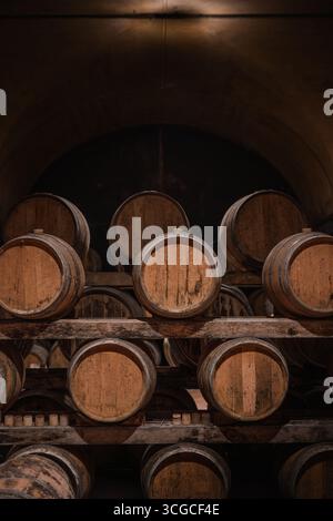 Eichenfässer, die in einem Alterskeller aufgereiht sind, warten darauf, Wein zu erhalten. Ein Bild, das die eindrucksvolle und traditionelle Atmosphäre des Weinbaus einfängt. Stockfoto