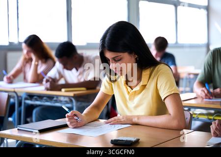 Konzentrierter Schüler, der eine Prüfung im Klassenzimmer mit Rechner und Notizbuch ablegt Stockfoto