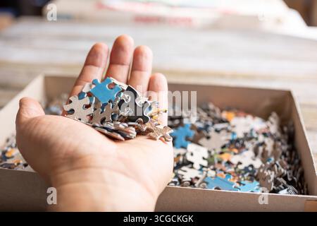 Eine Ansicht einer Hand, die einen Stapel Puzzleteile über die Puzzletasche mit den restlichen Teilen hält. Stockfoto