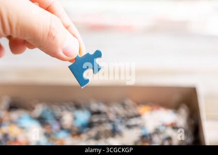 Eine Ansicht einer Hand, die ein blaues Puzzleteil über einem Karton voller Stücke hält. Stockfoto