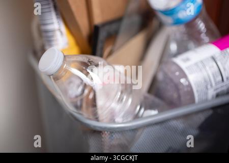 Eine Nahaufnahme einer nicht beschrifteten Plastikwasserflasche, Teil mehrerer Müllstücke in einem überfüllten Mülleimer. Stockfoto