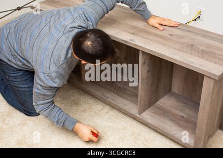 Blick auf eine Person, die ein hölzernes Unterhaltungszentrum in einem Wohnzimmerbereich baut. Stockfoto