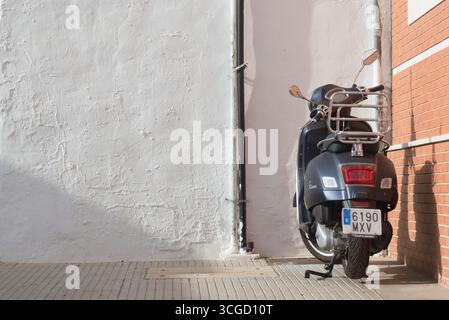 Blaues Vespa-Motorrad in Metallic-Optik, das auf dem Gehweg vor einer weißen Wand geparkt ist Stockfoto
