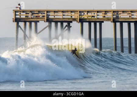 Amelia Island Surfer am Amelia by the Sea Pier, der auf einer großen Welle durch Hurrikan Erin Hunderte von Meilen vor der Küste im Nordosten Floridas reitet. Stockfoto