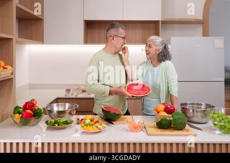 Fröhliches Senior asiatisches Paar teilt einen glücklichen Moment, um lebendiges frisches Obst und Gemüse in einem hellen modernen Hausküche gesunde Mahlzeit Konzept zuzubereiten Stockfoto