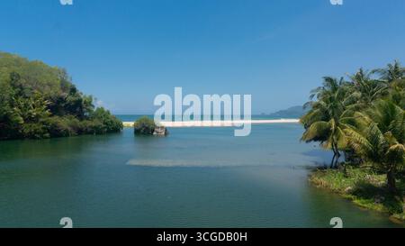 Ruhige tropische Landschaft mit einer ruhigen Lagune, die mit einem unberührten Sandstrand und Meer verschmilzt, umgeben von lebhaften Palmen und üppigem Dschungel unter Stockfoto